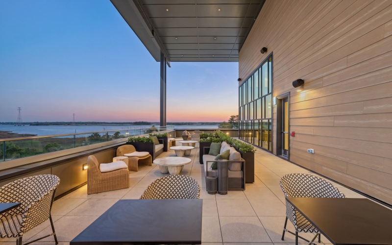 a patio with tables and chairs and a body of water in the background